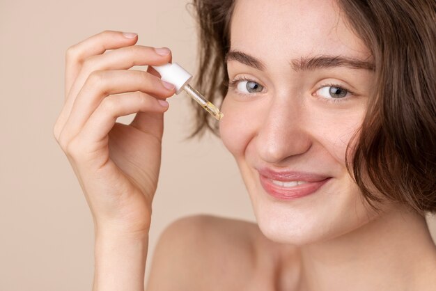 Fille souriante vue de côté à l'aide de sérum pour le visage