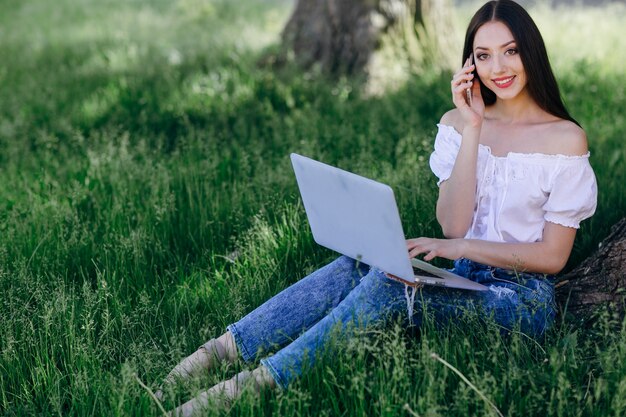 Fille sourire tout en parlant au téléphone et avoir un ordinateur portable