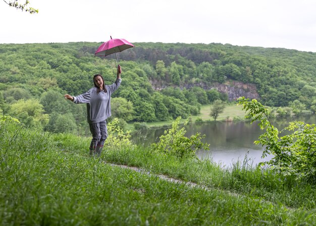 Une fille sous un parapluie sautant près d'un lac dans une région montagneuse par temps de pluie.