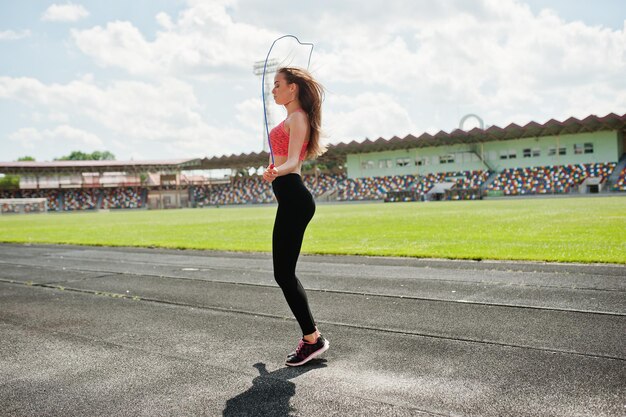 Fille sportive de remise en forme en tenue de sport dans un stade de football sports de plein air Heureuse femme sexy séance d'entraînement et saut avec corde