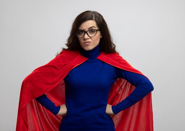 Fille de super-héros caucasien en colère avec cape rouge dans des lunettes optiques met les mains sur la taille