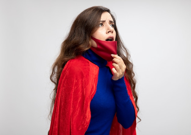 Fille de super-héros caucasien étouffant avec cape rouge portant et tirant un masque de protection rouge