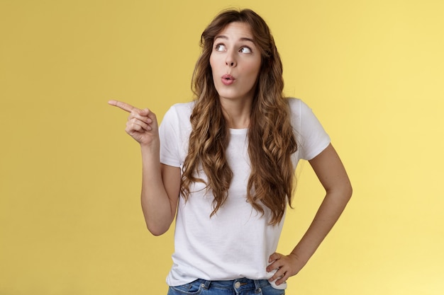 Une fille surprise admire l'offre géniale plie les lèvres intriguée le son wow observe une scène intéressante pointant du doigt regardant curieusement le coin supérieur gauche de la caisse une promo sympa montrant à un ami un nouveau menu café préféré