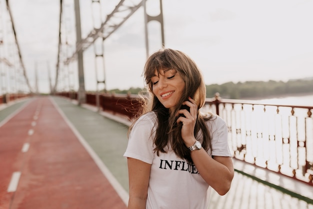 Fille en t-shirt blanc touchant ses cheveux et fermant les yeux en marchant