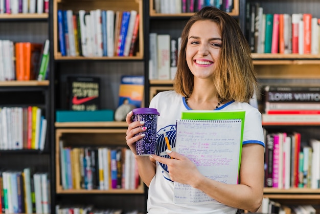 Fille tenant des bloc-notes et une tasse à café souriante