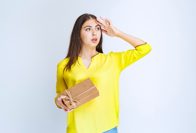 Fille tenant une boîte-cadeau en carton et semble confuse ou réfléchie.