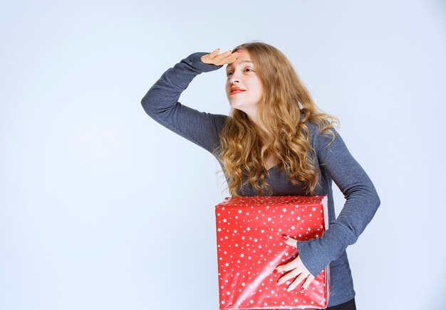 Fille tenant une boîte-cadeau rouge et à la recherche de quelqu'un.