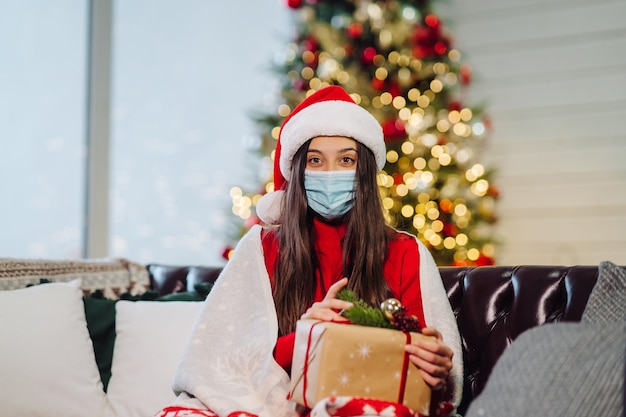 Fille tenant un cadeau de Noël le soir du Nouvel An. Fille regardant la caméra. Noël pendant le coronavirus, concept