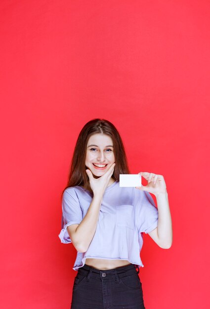 Fille tenant une carte de visite et a l'air surprise et excitée.