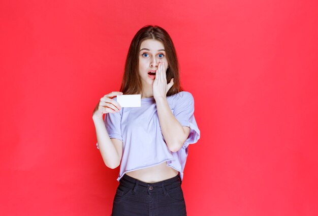 Fille tenant une carte de visite et a l'air surprise et excitée.