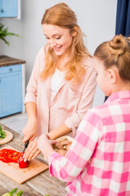 Photo gratuite fille tenant un champignon dans la main en regardant sa mère coupe le poivron avec un couteau sur la table