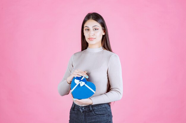 Fille tenant un coffret cadeau en forme de coeur bleu et le démontrant