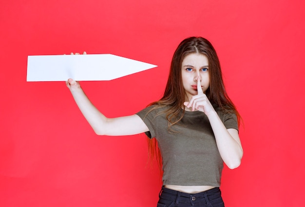 Fille tenant une flèche pointant vers la droite et demandant le silence.