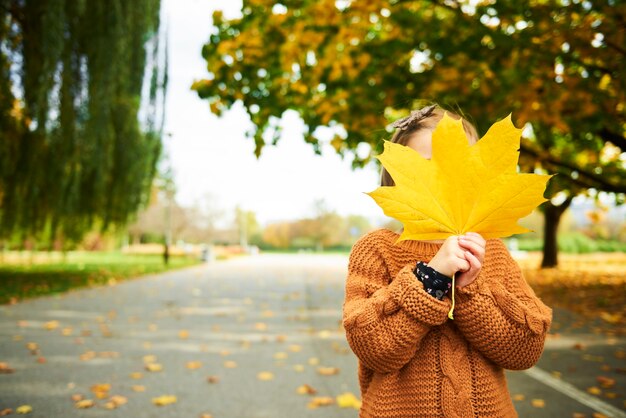 Fille tenant une grande feuille d'automne devant son visage