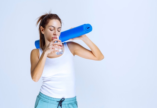 Fille tenant un tapis de yoga bleu et un verre d'eau.