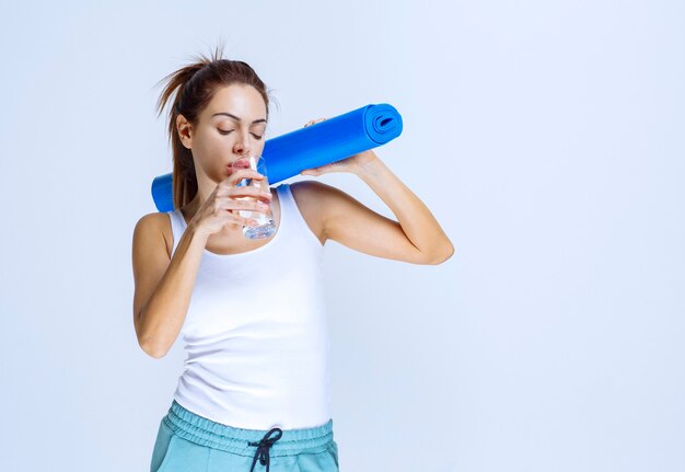 Fille tenant un tapis de yoga bleu et un verre d'eau.