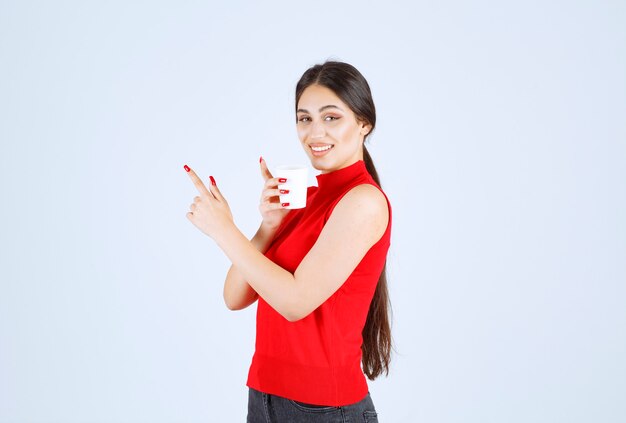 Fille tenant une tasse de café blanche et la pointant du doigt.