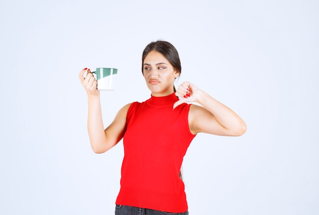 Fille tenant une tasse de café et montrant le pouce vers le bas.