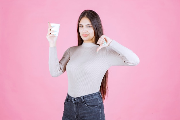 Fille tenant une tasse de café et montrant le signe du pouce vers le bas