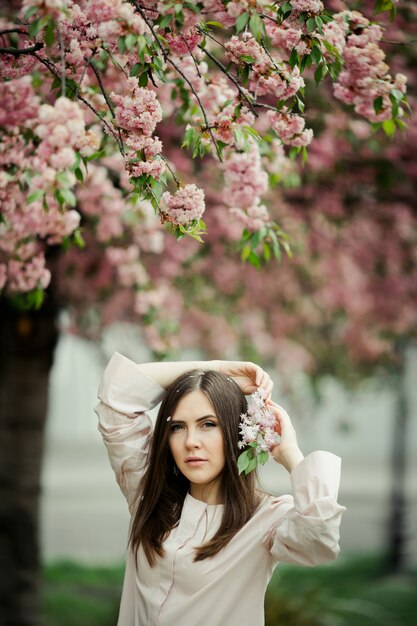 Fille tient les mains derrière la tête avec une branche de sakura