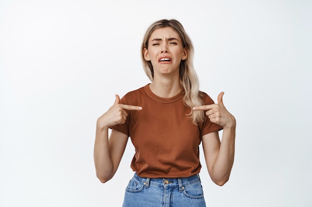 Photo gratuite fille triste et misérable se pointant du doigt en pleurant, sanglotant, debout sur blanc