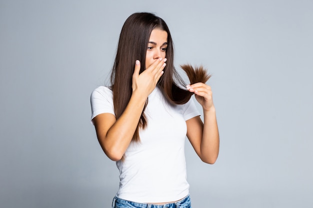 Fille triste en regardant ses cheveux abîmés isolé sur blanc