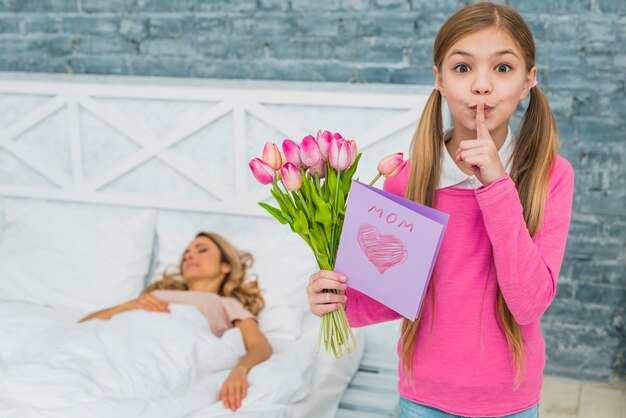 Fille avec des tulipes et carte de voeux tenant un doigt sur les lèvres