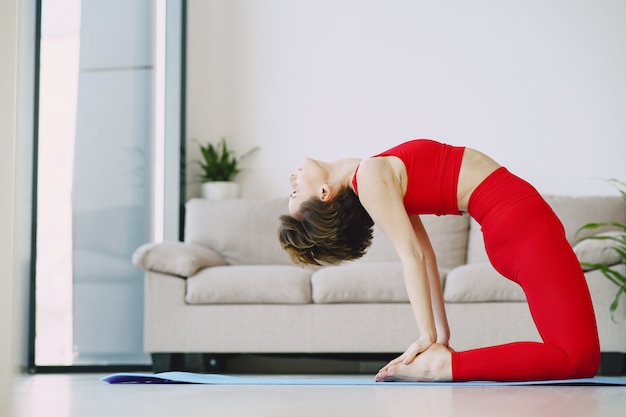 Fille en uniforme de sport rouge pratiquant le yoga à la maison