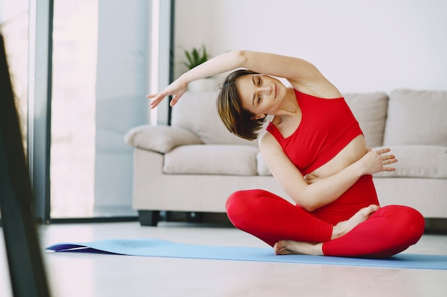 Fille en uniforme de sport rouge pratiquant le yoga à la maison