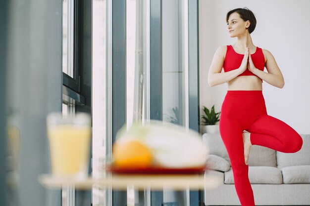 Fille en uniforme de sport rouge pratiquant le yoga à la maison