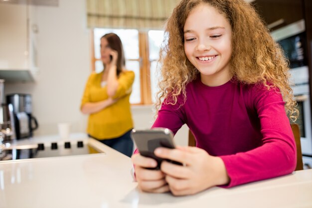 Fille utilisant un téléphone portable dans la cuisine