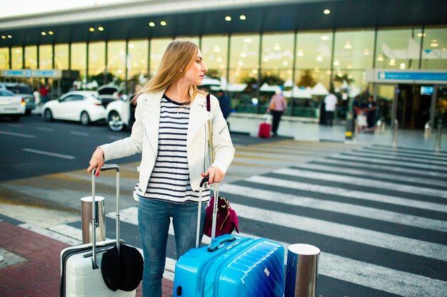 Une fille en veste blanche est en train de traverser avec des valises bleues et blanches