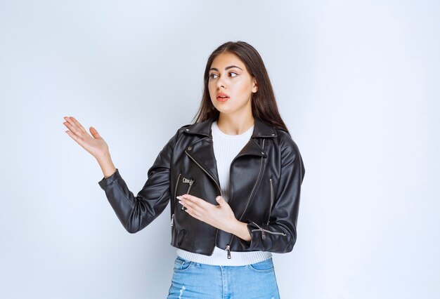 Fille en veste de cuir présentant quelqu'un de côté.