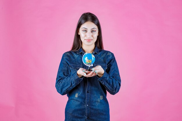 Fille en veste en jean tenant un mini globe dans sa paume