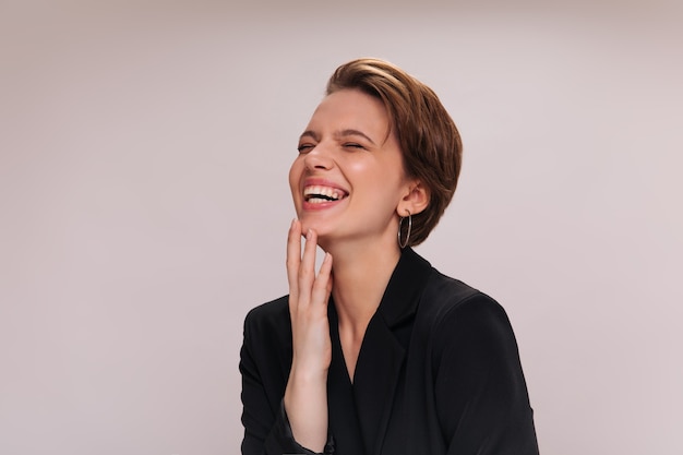 Fille en veste noire riant sur fond isolé. Gros plan à l'intérieur du portrait de femme en costume sombre souriant et posant sur fond blanc