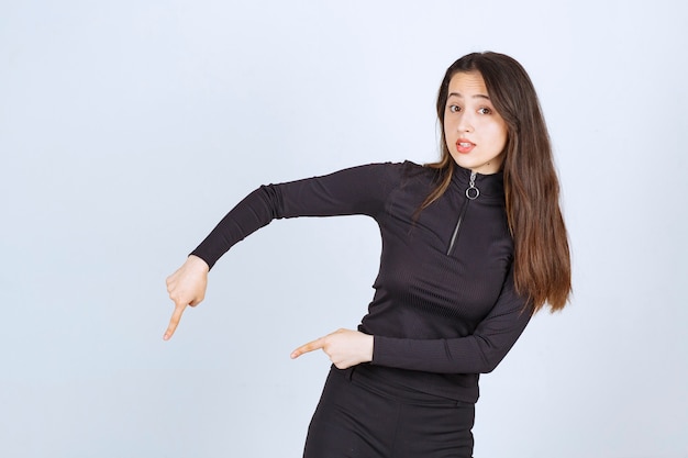 Fille en vêtements noirs pointant ci-dessous.