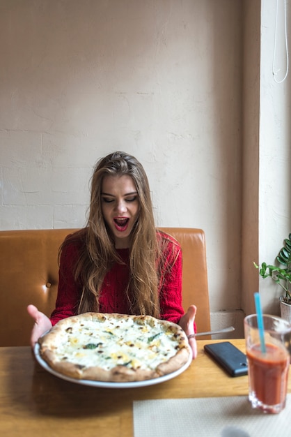 Fille avec le visage drôle tenant une pizza au fromage