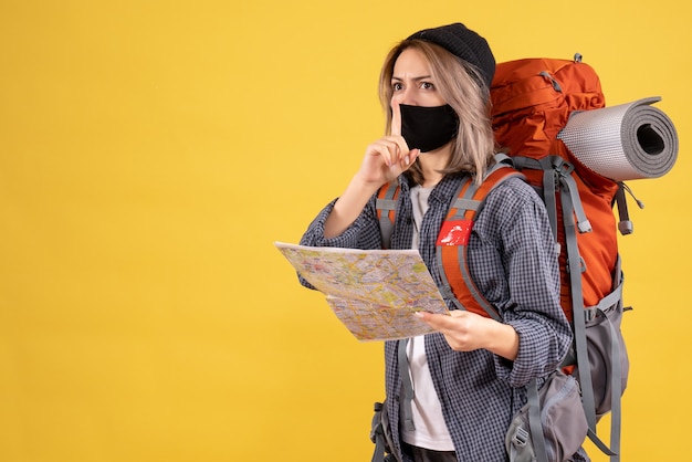 fille de voyageur avec masque noir et sac à dos tenant une carte faisant signe de silence