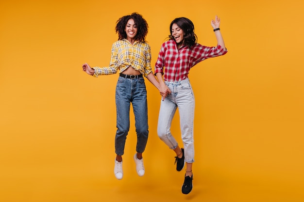 Filles actives positives avec la danse des cheveux ondulés foncés. Les femmes rient et apprécient les séances photo