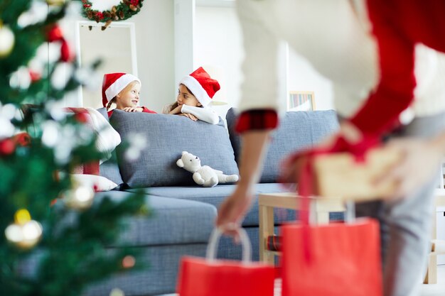 Des filles cachées regardant leurs parents mettre des cadeaux de Noël sous le sapin