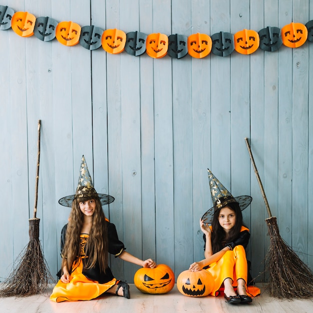 Photo gratuite des filles en costumes de sorcière et des chapeaux pointus assis près d'une clôture