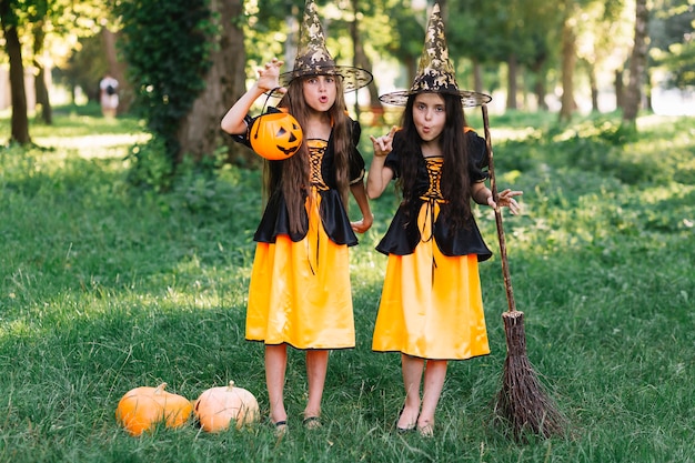 Filles en costumes de sorcière faisant des grimaces tenant un balai et une citrouille
