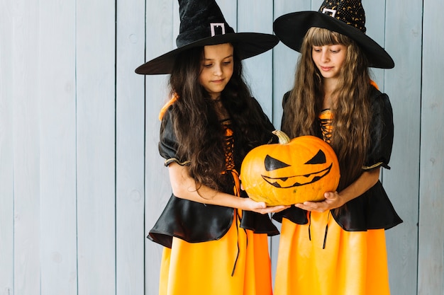 Photo gratuite filles en costumes de sorcière tenant et regardant la citrouille