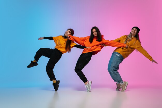 Filles dansant le hip-hop dans des vêtements élégants sur fond de studio dégradé en néon.