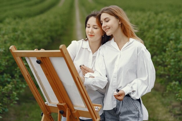 Filles élégantes et belles peignant dans un champ