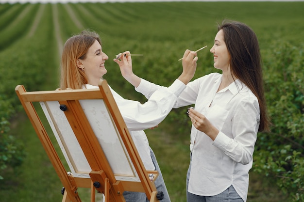 Photo gratuite filles élégantes et belles peignant dans un champ