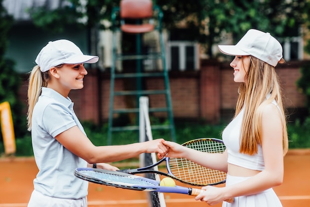 Photo gratuite des filles heureuses jouant au tennis, serrant la main, souriantes, passent du temps ensemble.