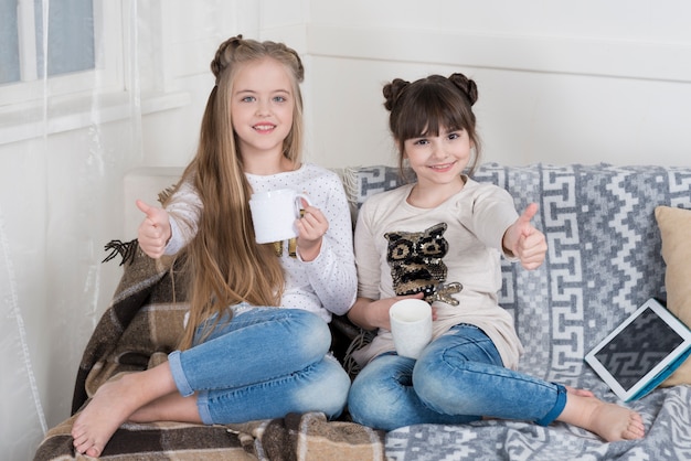 Photo gratuite filles heureux sur le canapé avec des tasses