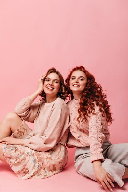 Filles inspirées posant sur le sol avec un sourire sincère. Photo de Studio d'amis heureux sur fond rose.