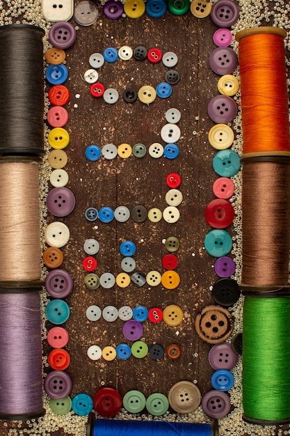 Fils à coudre avec des boutons colorés en plastique formant bonjour mot sur une table rustique marron